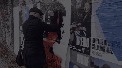 Pasting the Breche die Grenzen poster onto a wall in Berlin