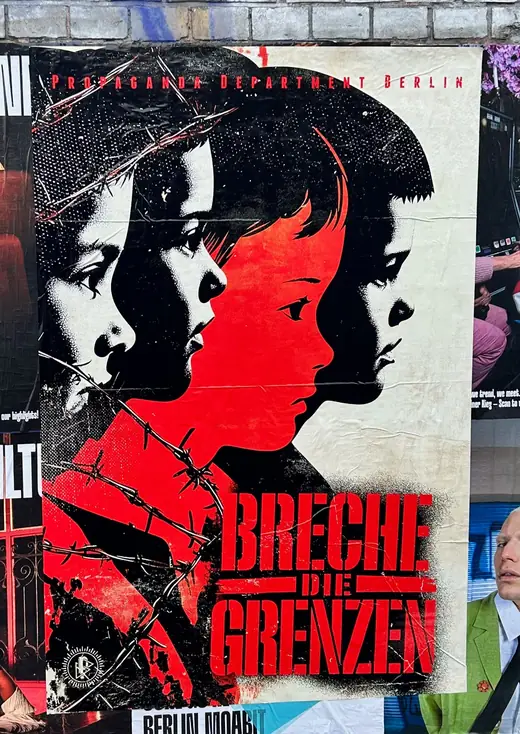 The poster: children behind barbed wire under the red words Breche die Grenzen