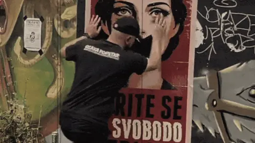 Pasting the Borite se za svobodo medijev poster onto a painted wall in Ljubljana