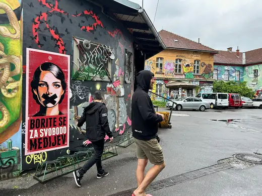 The finished poster on a graffiti-covered wall in Ljubljana, with people walking past