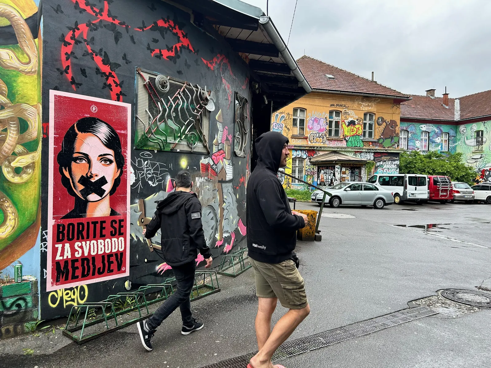 The finished poster on a graffiti-covered wall in Ljubljana, with people walking past
