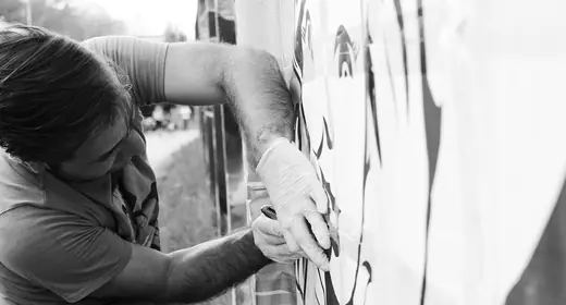 black and white photo showing a man cutting part of the stencil directly on the wall