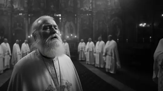 An old bearded priest singing, the clergy behind him